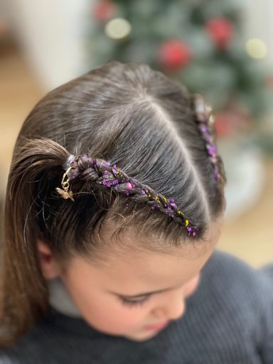 Niña con cabello dividido en dos secciones y decoraciones de colores en el peinado.