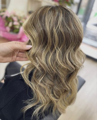 Cabello ondulado y rubio con reflejos, peinado sobre un fondo suave y floral.