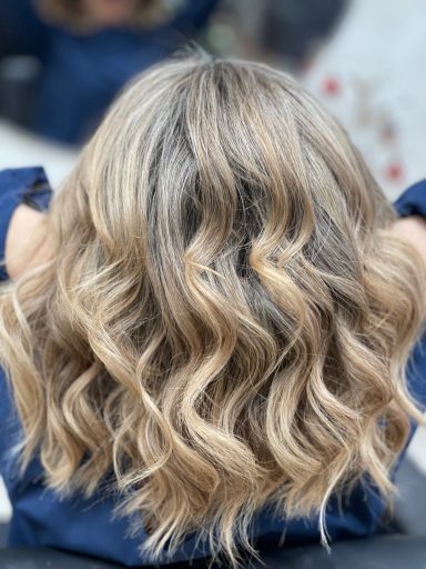 Mujer con cabello largo, ondulado y rubio, visto desde atrás.