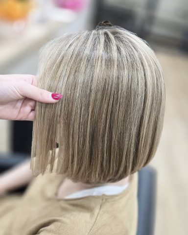 Corte de cabello bob rubio con textura en la parte superior. Mano sujetando el pelo.