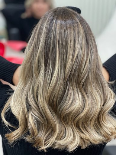 Mujer con cabello largo y ondulado en tonos rubios, vista desde atrás.