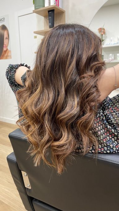 Cabello ondulado y brillante, largo, con un tono castaño claro en un entorno de salón.